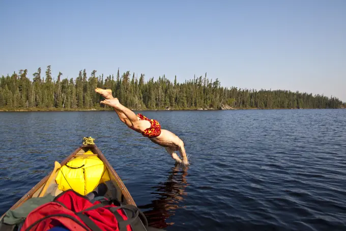 A man cooling off and diving into a lake on a hot day while canoeing and camping in Wabakimi Provincial Park, Ontario, Canada