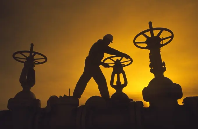 Oil industry worker turning valve on pipeline