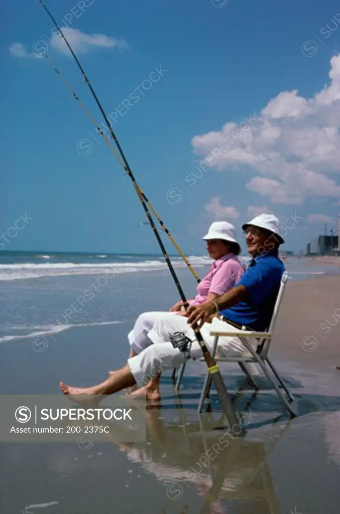 Senior couple sitting on beach chairs with fishing rods