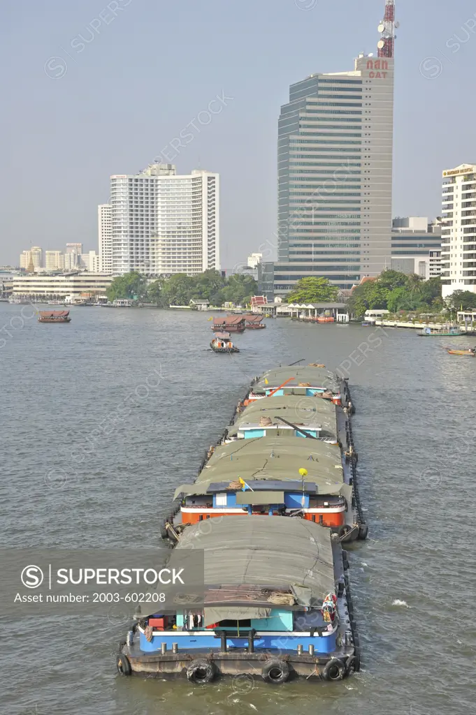 High angle view of four rice barges being pulled by a tugboat in a river, Chao Phraya River, Bangkok, Thailand