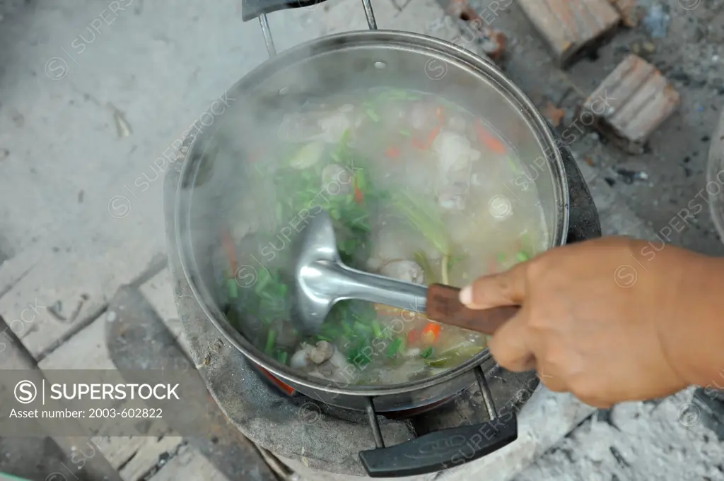 Thailand, Khon kaen, Cooking Spicy Chicken Soup (Tom Yum Gai) over charcoal fire in back yard