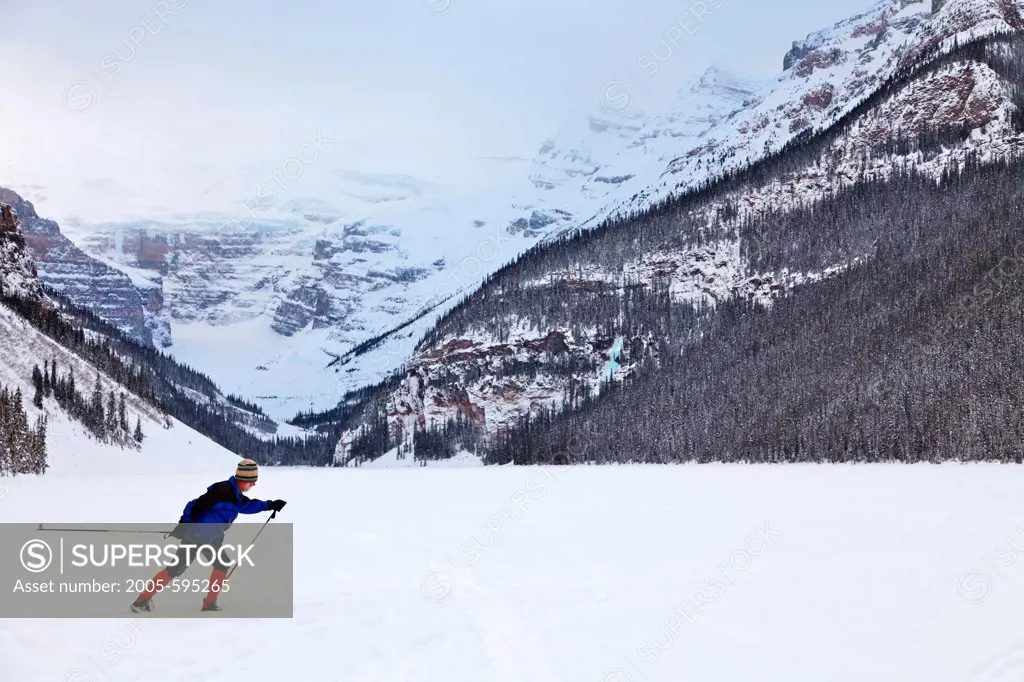 Cross-country skier skiing on Lake Louise below Mt Victoria, Mt Victoria, Banff National Park, Alberta, Canada