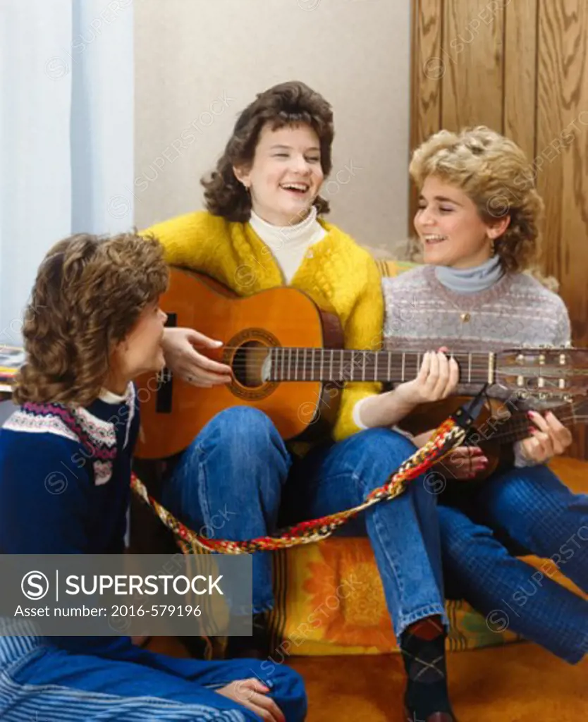 Three teenage girls sitting together and playing a guitar