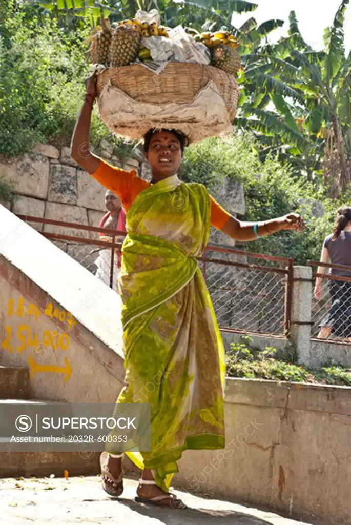Female fruit seller carrying a basket of pineapples on head, Hampi, Karnataka, India