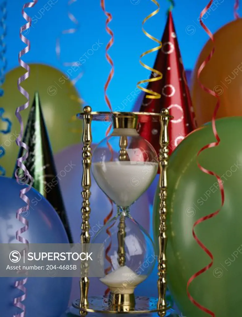 Close-up of an hourglass with balloons and party hats