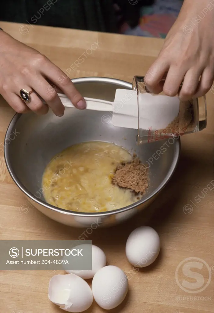 Close-up of a person's hands pouring cocoa powder into a bowl of beaten eggs