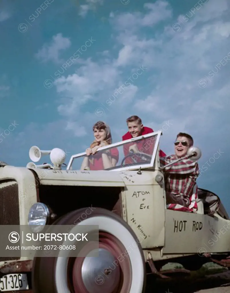 Low angle view of two teenage boys and a teenage girl in a vintage car, 1955