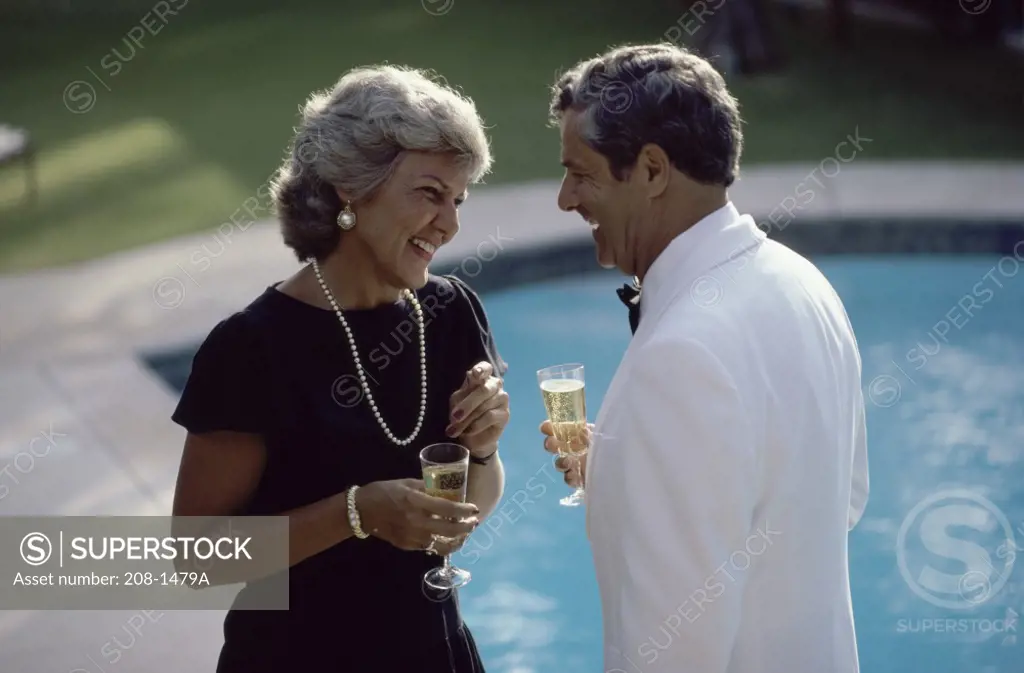 Mature couple holding champagne flutes at poolside