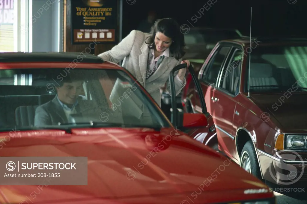Young salesperson looking at a young man sitting in a car in a showroom