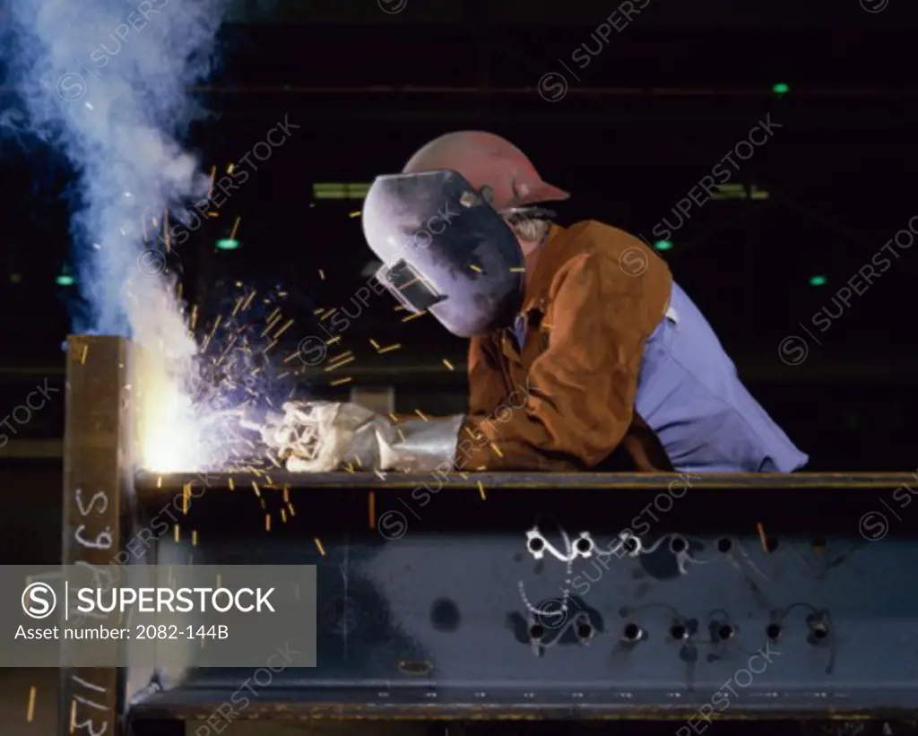 Worker wearing a welding mask welding metal beams