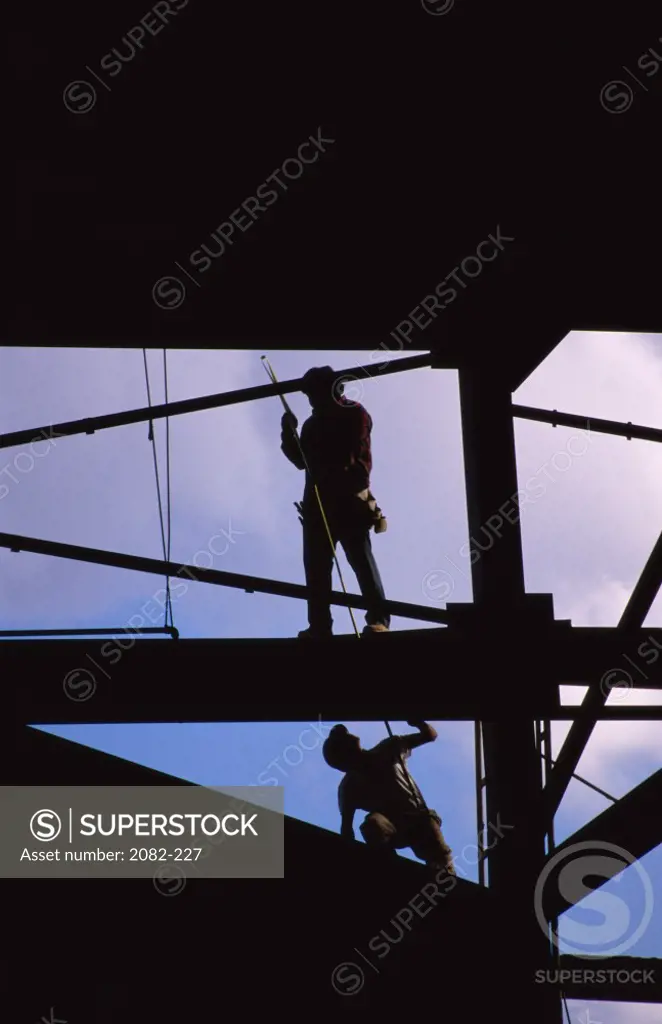 Silhouette of steel workers, walking on metal beams