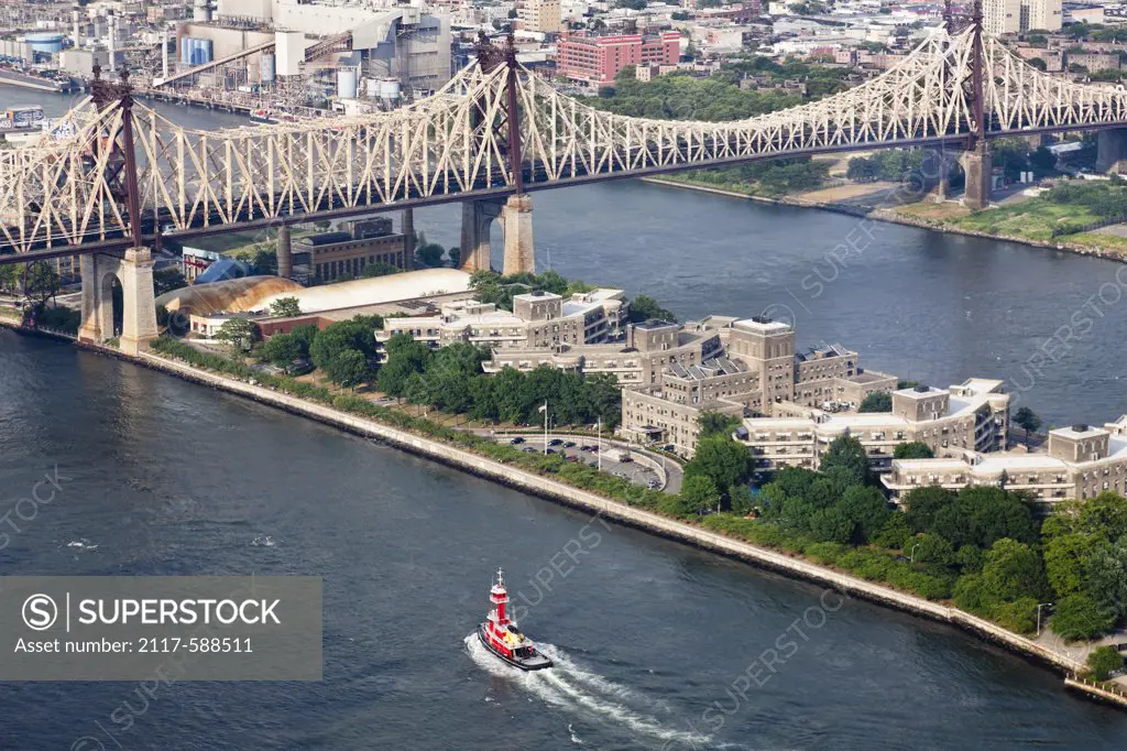 USA, New York City, Tugboat cruising up East River along Roosevelt Island and 59th Street Bridge
