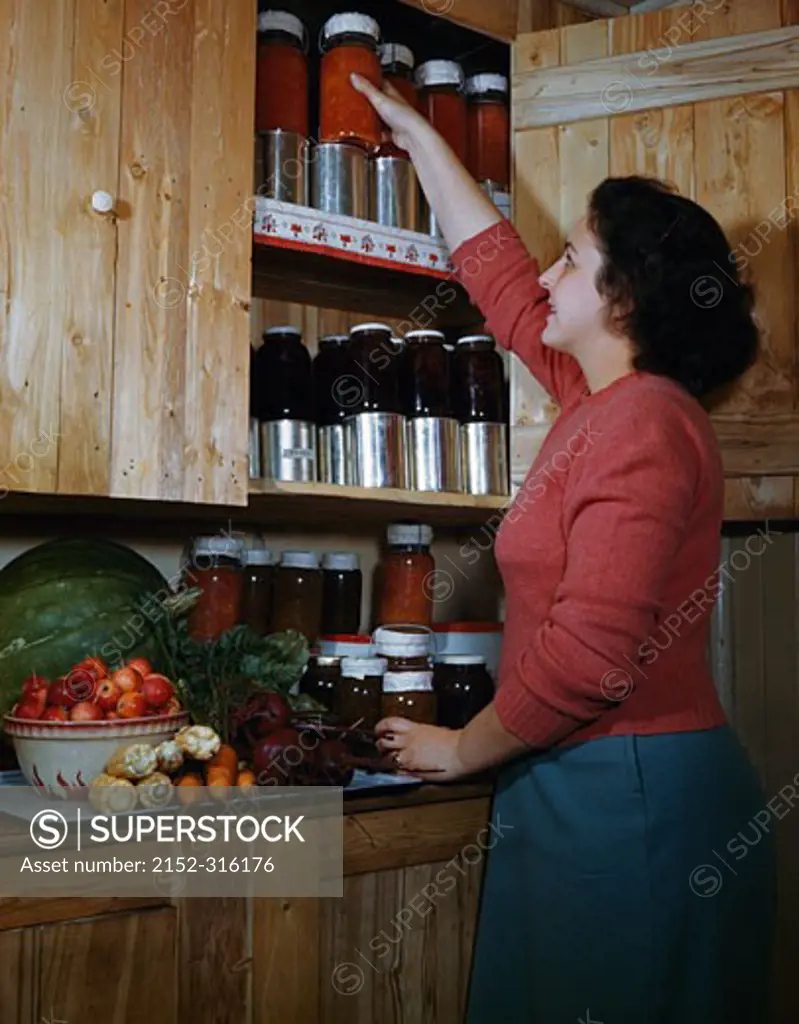 Young woman removing jar from kitchen cupboard