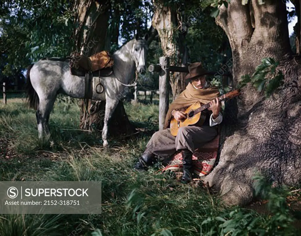 Gaucho man playing a guitar with a horse standing beside him, Argentina