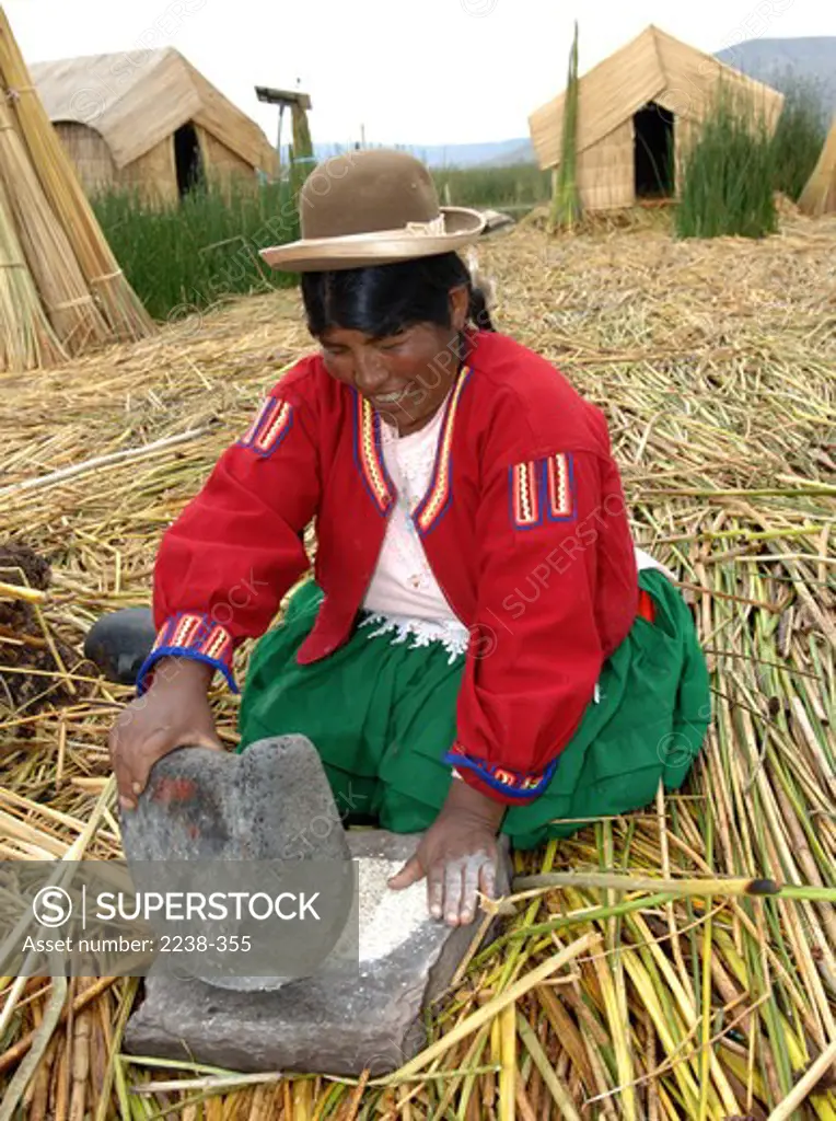 Aymara woman grinding wheat on a stone, Uros, Lake Titicaca, Puno, Peru