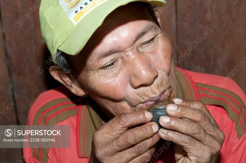 Makuna man, Joao 70 yrs, playing a small hand-made whistle. Sao Pedro, Rio Tiquie, Amazonas, Brazil, 11-9-12
