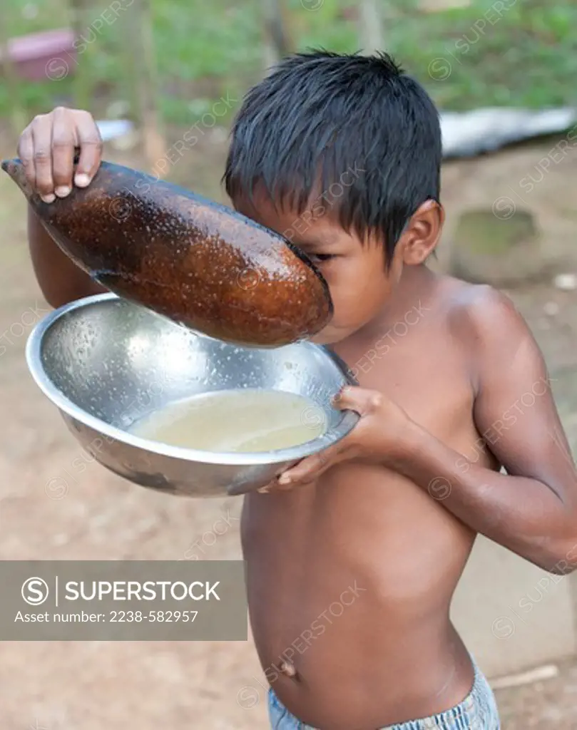 Tukano boy drinking tapioca porridge (mingau) prepared from manioc. The porridge consists of goma (tapioca), warm water, and a little manioc flour. Mingau is typically served at breakfast. Johnny, 7 yrs, is using a bowl fashioned from a calabash gourd (Crescentia cujete) to scoop up the porridge. Pirara-Poco, Tiquie River, affluent of the Uaupes, Amazonas, Brazil, 11-11-12