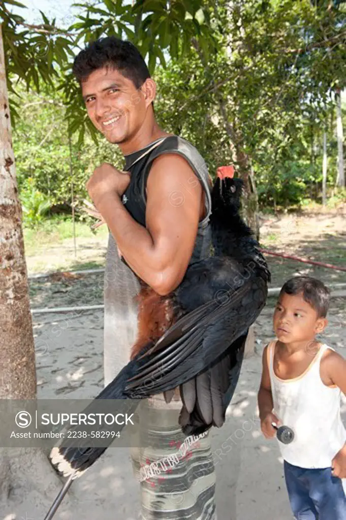 Hunter, Louis 32 yrs, with a razor-billed curassow (Mitu tuberosum) he has shot in the forest with a 20-bore shotgun. The curassow is known locally as mutum. The meat is eaten and the tail feathers are tied together to make dusters. Cacautuba, Tefe River, Amazonas, Brazil, 9-10-12