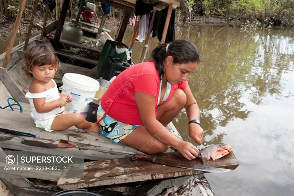 Slicing fish (ticando) so that it cooks through when roasting. Piranha caju (Serrasalmus nattereri). Grace, 24 yrs, and daughter Evia 1 yr. 9 months. Igarape Ubim, Lago Amana, Amazonas, Brazil, 9-19-12