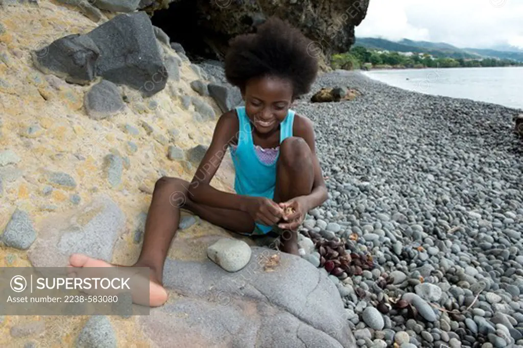 Fedwin (Haitian girl) 11 yrs breaking open the endocarps of tropical almond (Terminalia catappa) to eat the nuts on the shore of the Caribbean Sea. Rodney's Rock Beach, Jimmit, Dominica 12-17-12