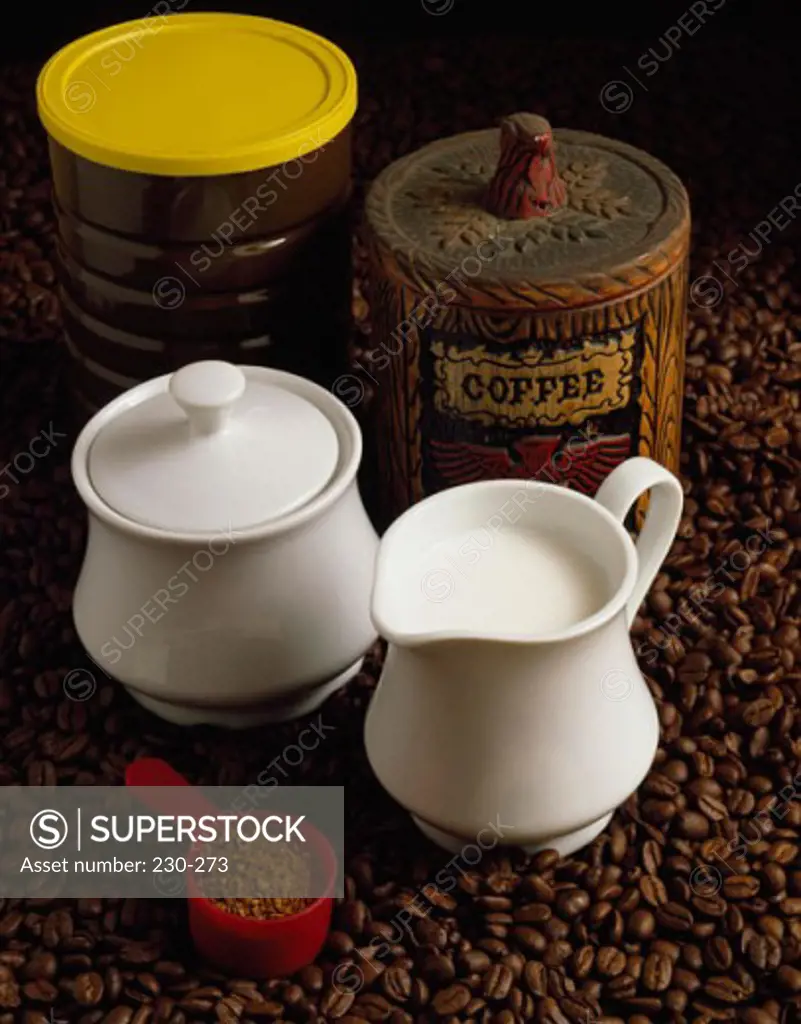 Close-up of a mug of milk with a measuring spoon and jars on coffee beans