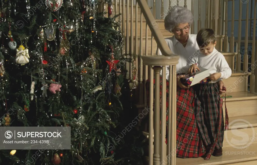 Senior woman with her grandson opening a Christmas present on a staircase