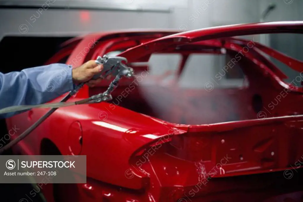 Person's hand spraying paint on a car in a car plant, General Motors Assembly Plant, St. Therese, Quebec, Canada