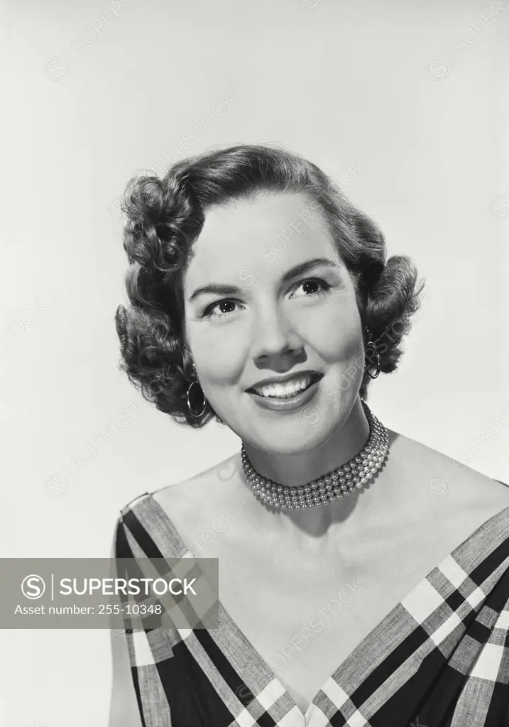 Vintage Photograph. Smiling woman with curly hair wearing deep V-neck blouse and pearl necklaces looking off camera
