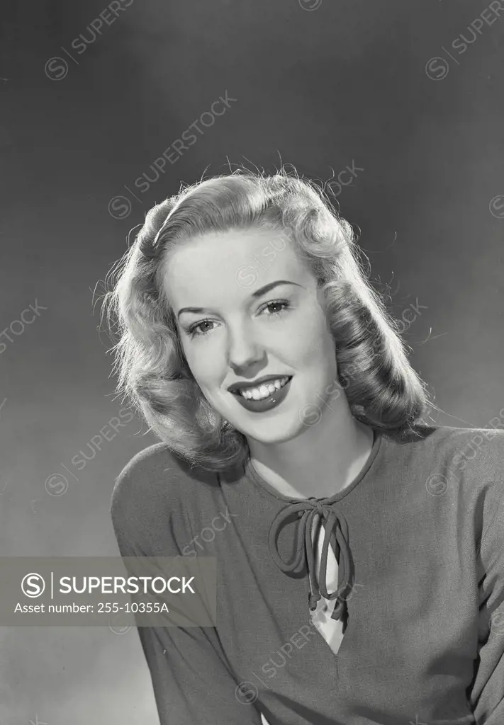 Blonde woman with wavy hair wearing blouse with tie in front smiling