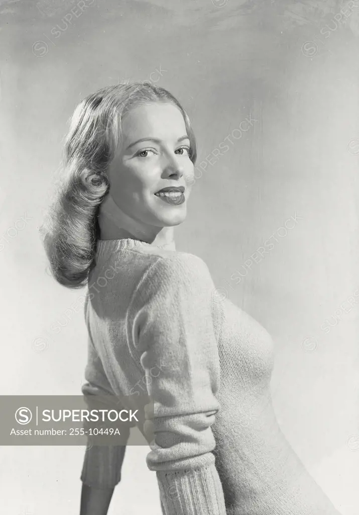 Blonde woman wearing sweater leaning back on arms turned to the side smiling