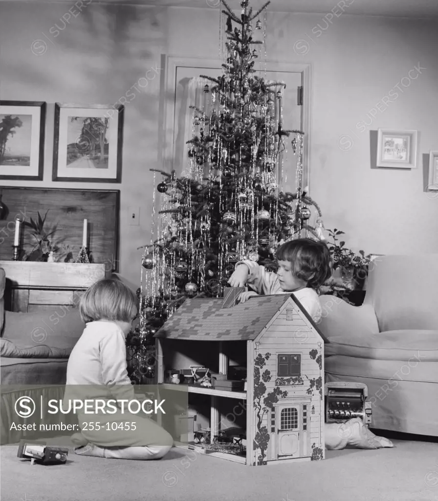 Side profile of two girls playing with a dollhouse near a Christmas tree