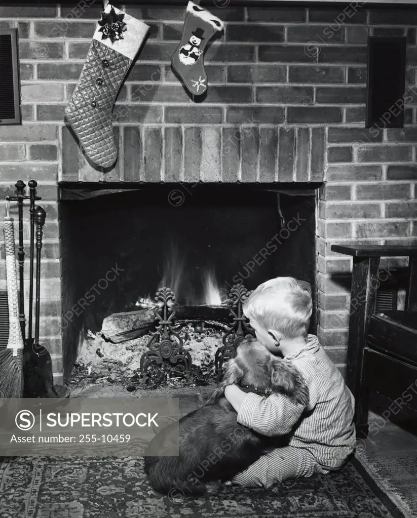 Boy sitting near fireplace with dog