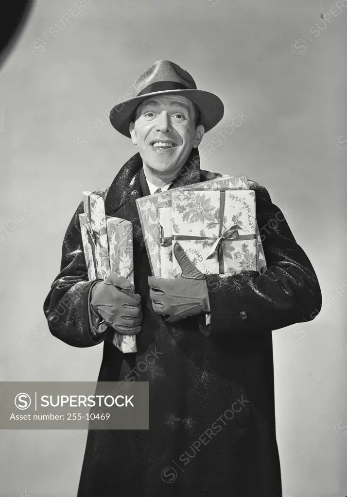 Vintage Photograph. Smiling man wearing hat and winter coat dusted with snow holding wrapped holiday presents