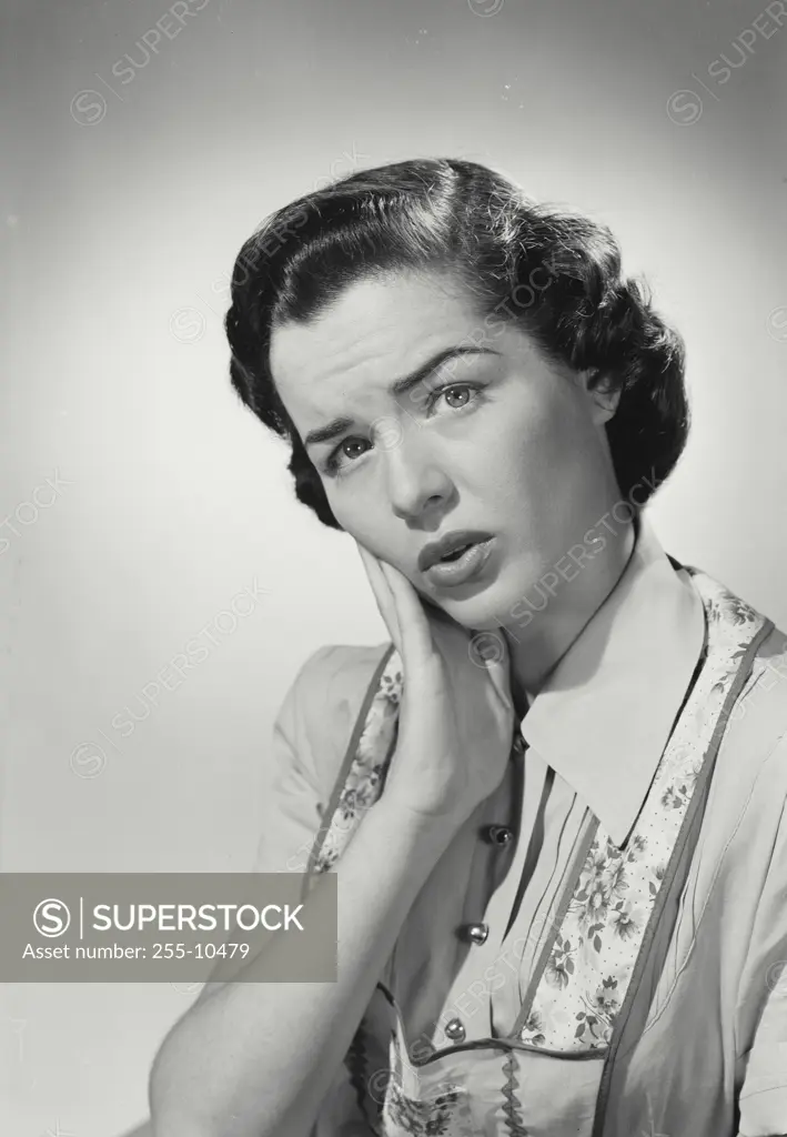 Vintage Photograph. Brunette woman wearing apron over blouse holding hand to cheek in discomfort