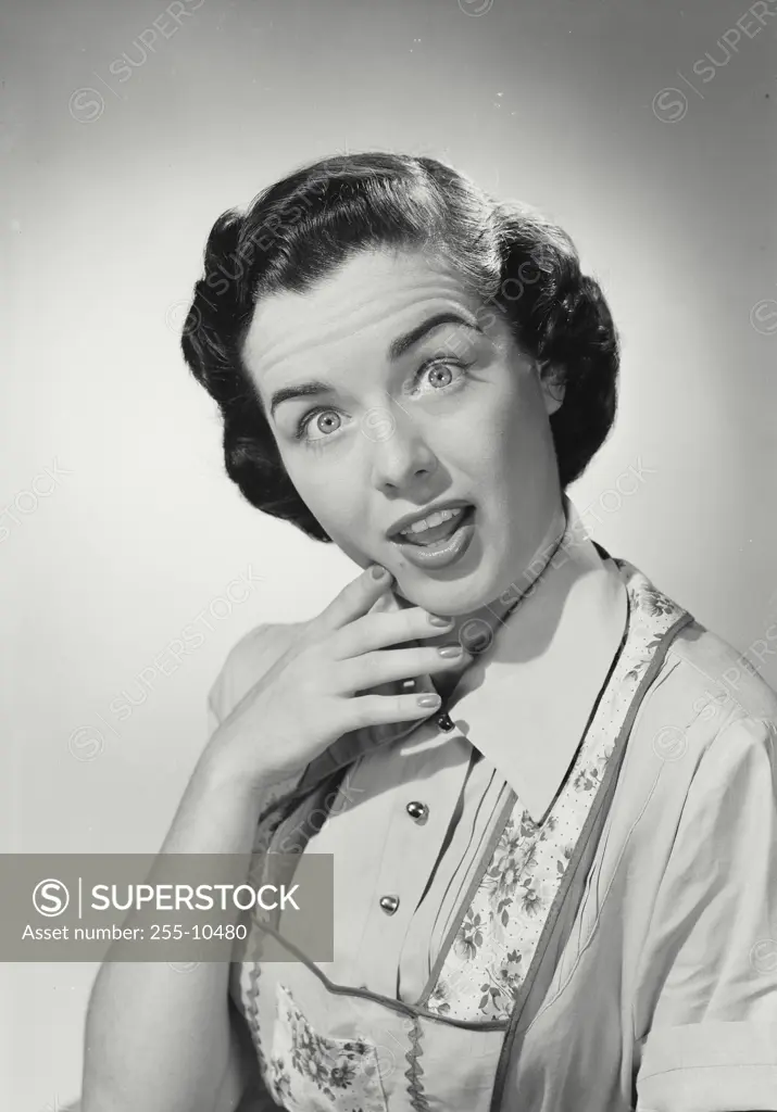 Vintage Photograph. Brunette woman wearing apron over blouse holding hand to chin with exaggerated surprised expression