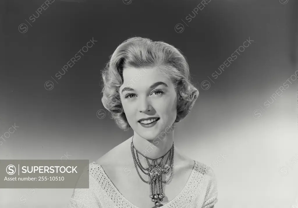 Vintage Photograph. Blonde woman smiling with curled hair wearing knit blouse with detailed necklace in front of gradated background