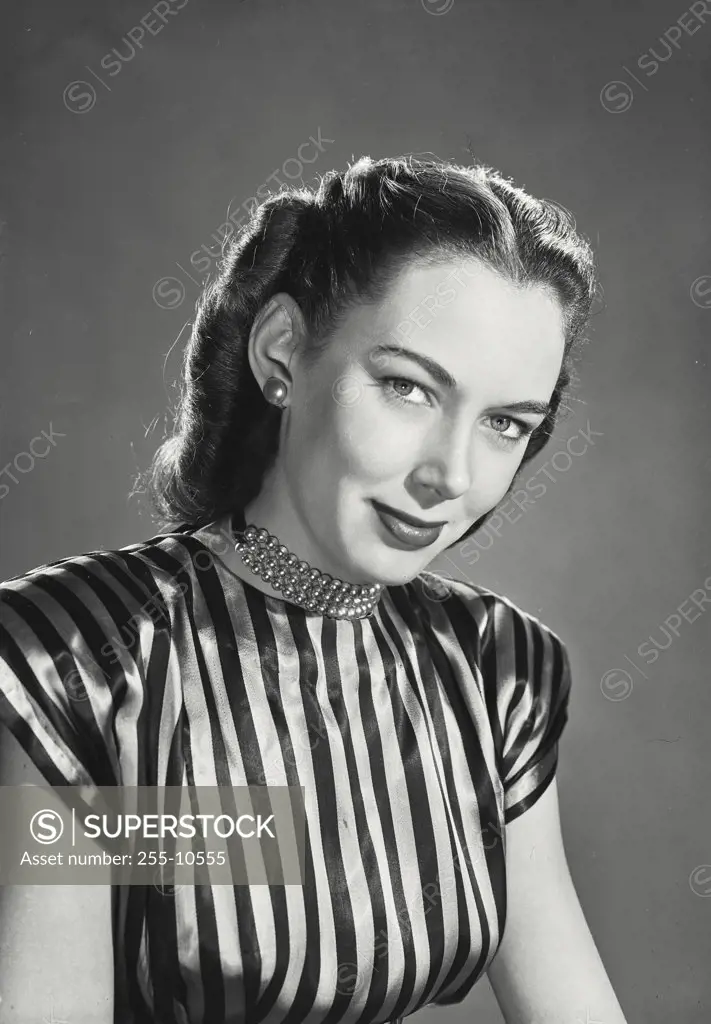 Brunette woman wearing striped silk blouse and beaded necklace with soft smile expression