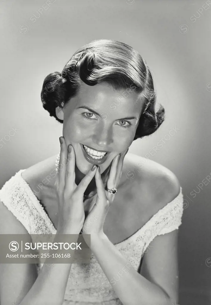 Vintage photograph. Portrait of smiling woman holding hands up to face.