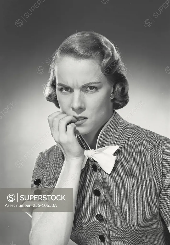 Vintage photograph. Woman in button blouse with bow biting fingernails.