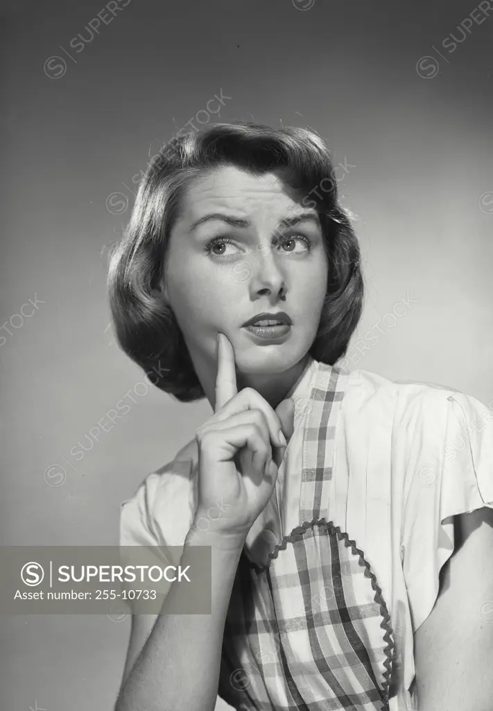 Vintage Photograph. Brunette woman with short hair wearing apron holding up index finger to cheek looking off camera