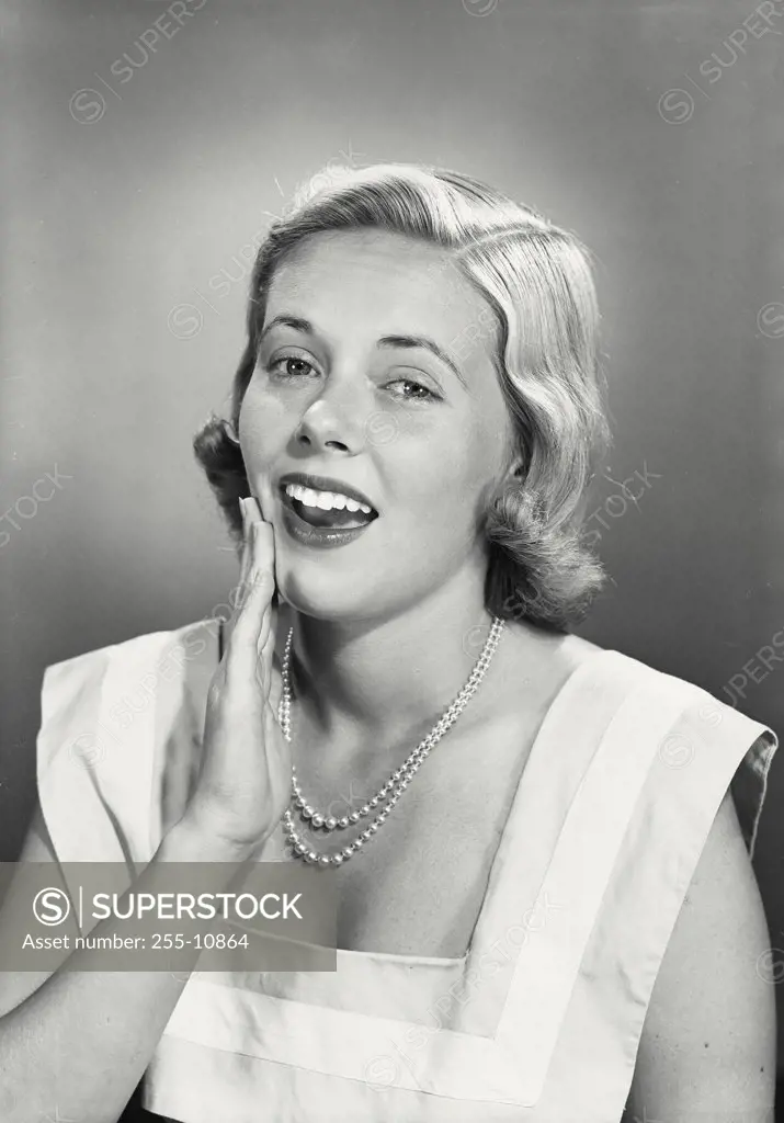 Vintage photograph. Portrait of blonde woman wearing pearl necklace with hand on cheek