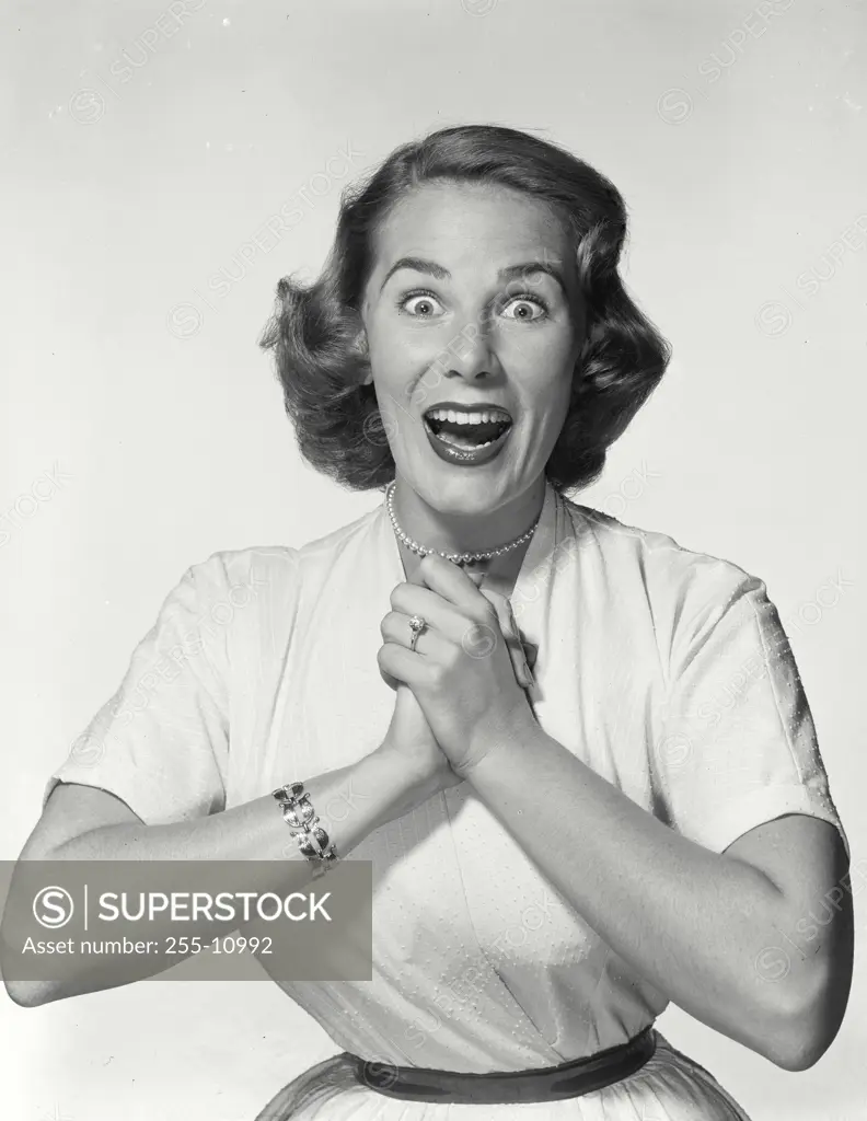 Vintage Photograph. Young woman wearing white dress clasping hands with surprised expression