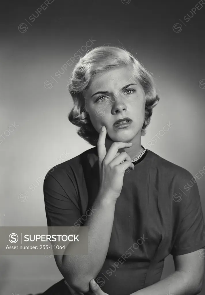 Vintage Photograph. Smiling young woman with short blonde hair wearing high collared blouse holding hand up to chin with puzzled look on face