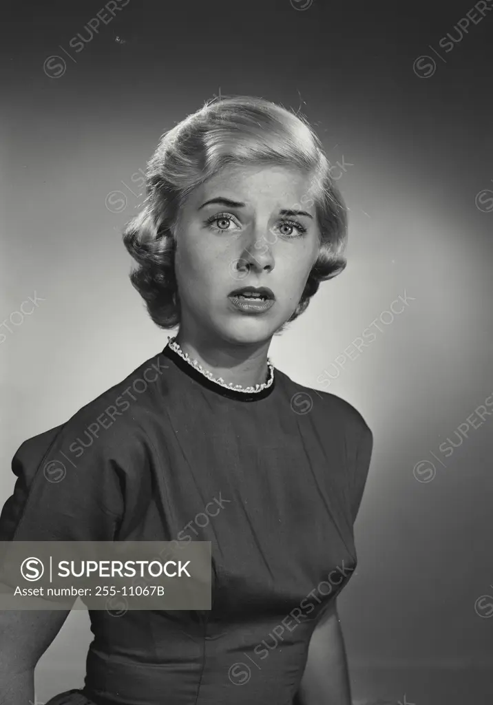 Vintage Photograph. Smiling young woman with short blonde hair wearing high collared blouse with apprehensive expression