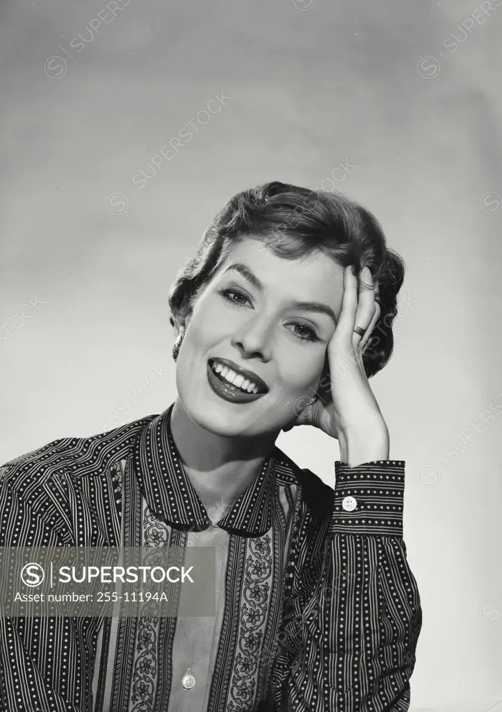 Vintage Photograph. Smiling woman with short hair wearing blouse with floral designs and stripes resting head on hand