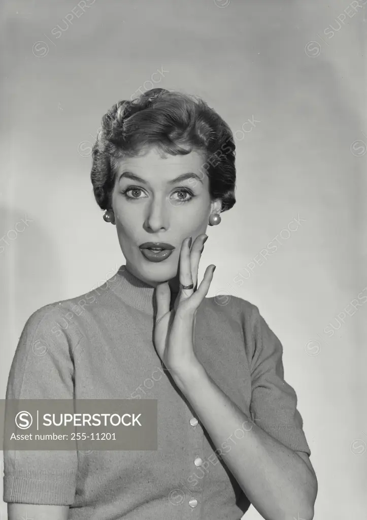 Vintage Photograph. Woman wearing button up sweater with hand raised near mouth with shocked expression