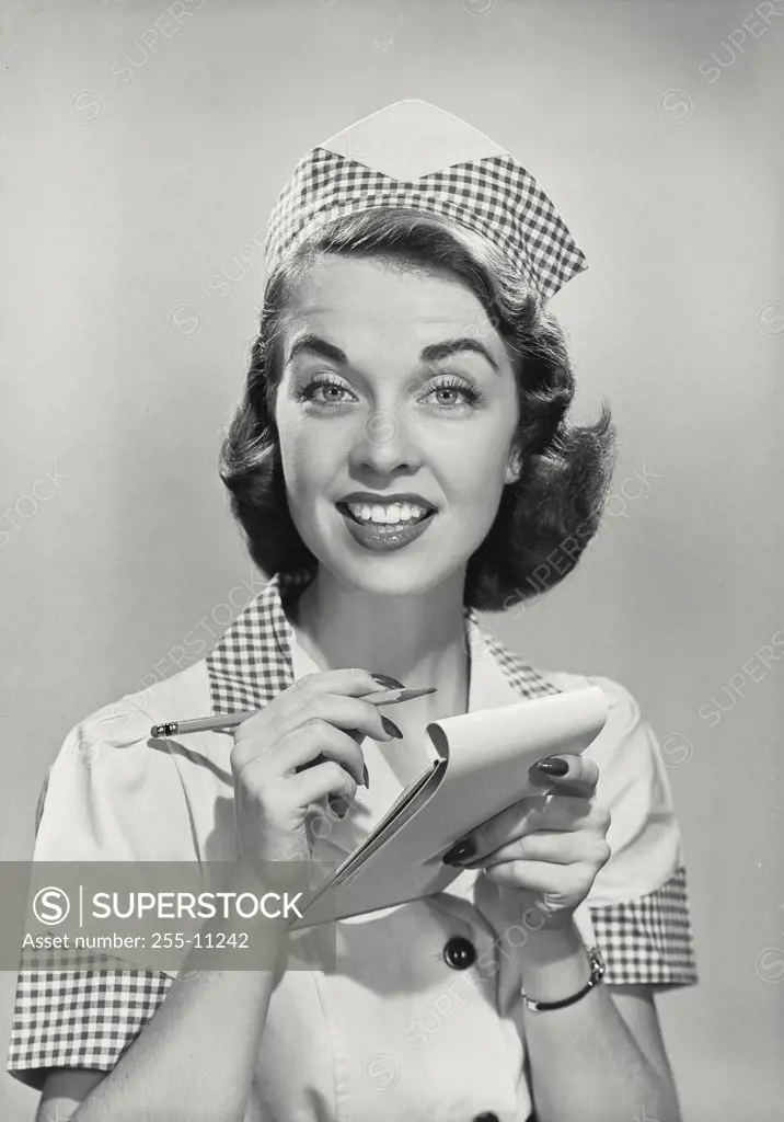 Vintage photograph. Brunette woman with raised eyebrows wearing waitress uniform with pencil and order pad