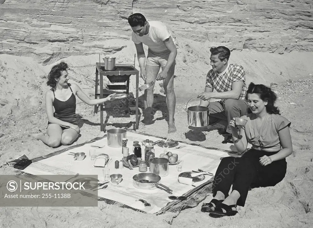 Vintage photograph. Two men and two women cooking on grill for picnic at the beach
