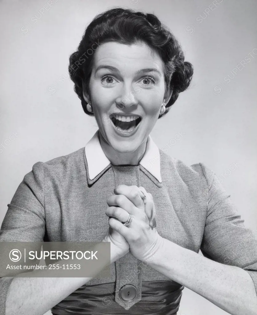 Portrait of a mid adult woman looking surprised with her hands clasped