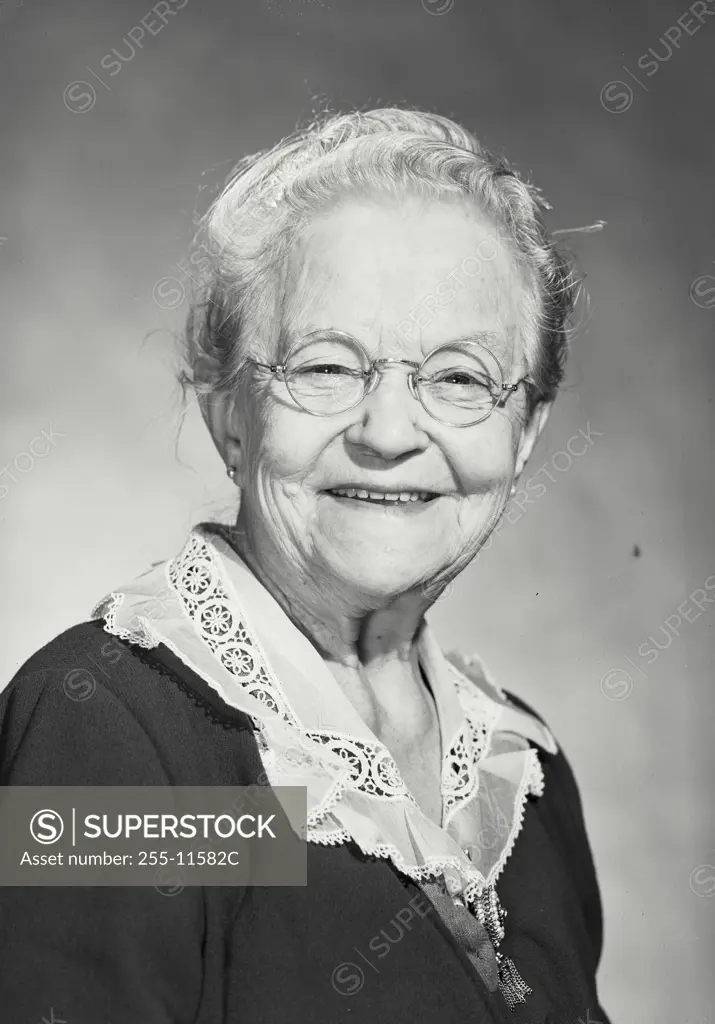 Vintage Photograph. Smiling elderly woman wearing glasses and blouse with lace collar looking at camera